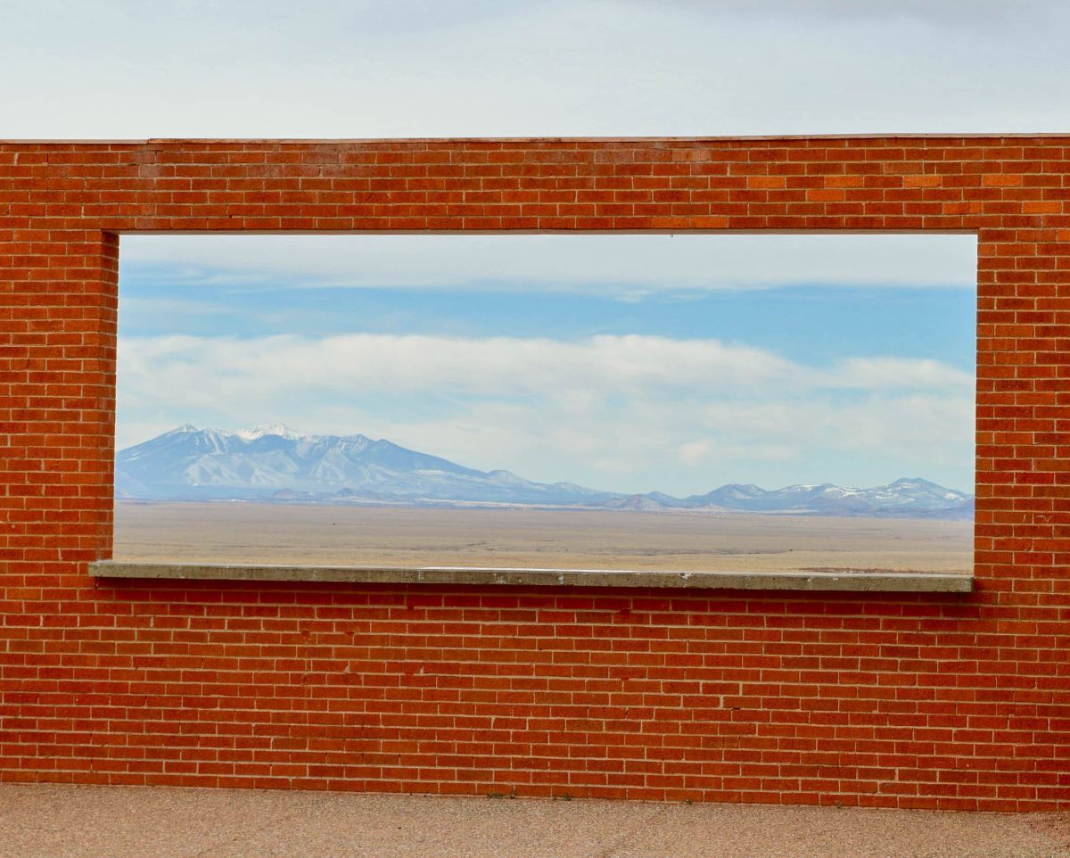 Brick wall with a large rectangular window cut out perfectly framing Arizona snowy mountains in the distance