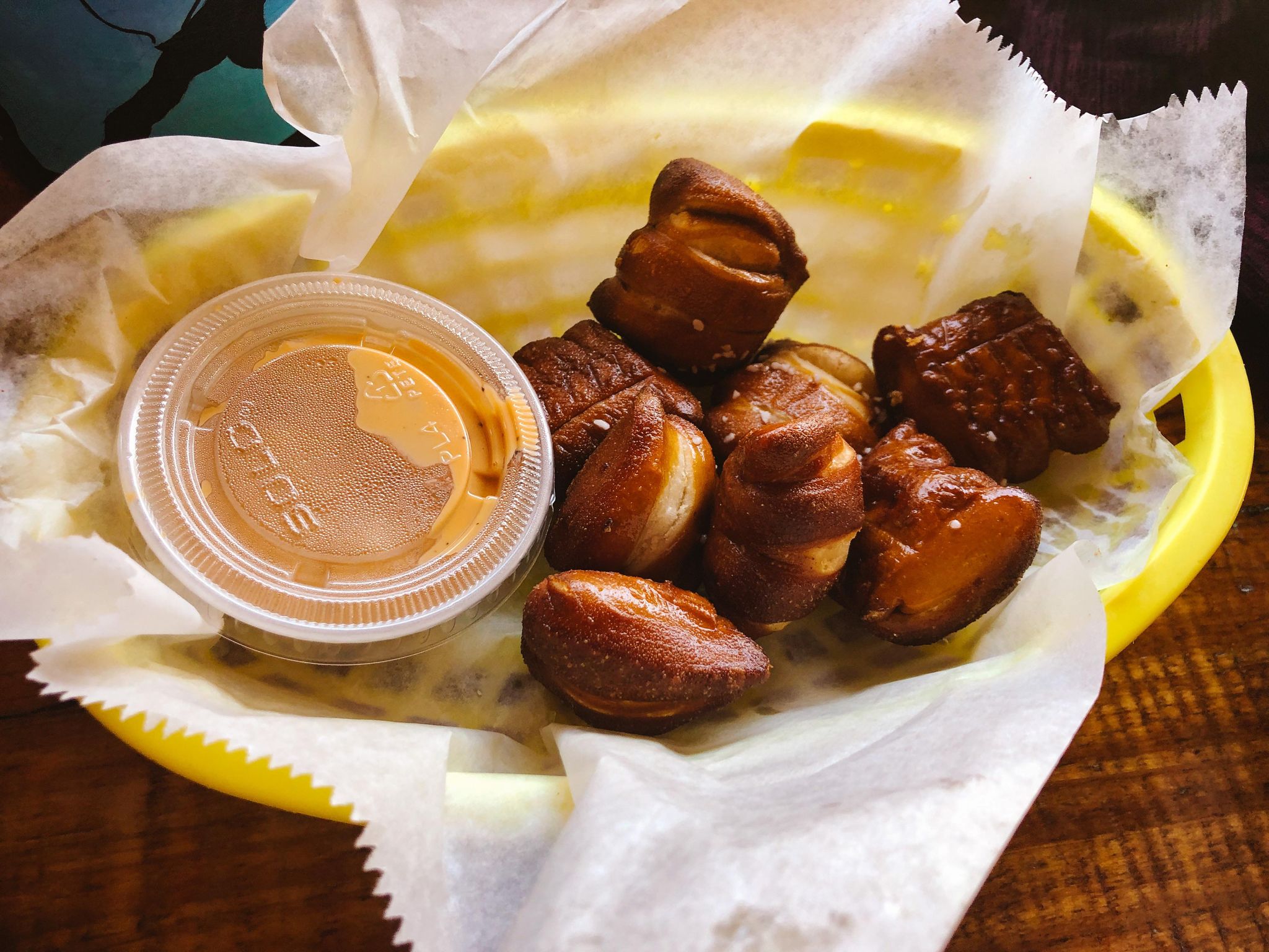 small pretzel bites in a yellow basket with orange beer cheese in a to-go container