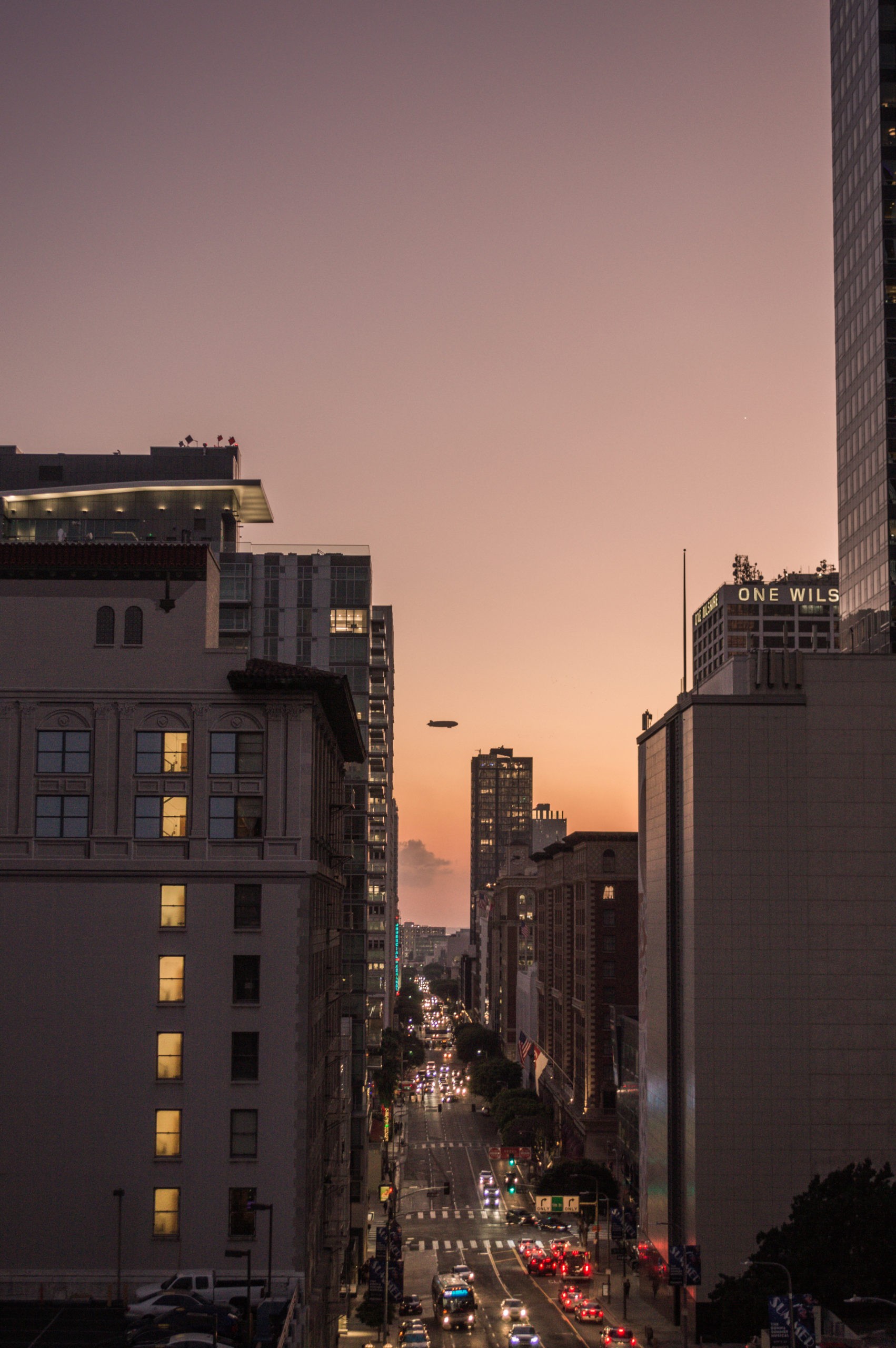 Downtown LA views at sunset with a plane flying between the buildings and cars with their headlights on driving along the road