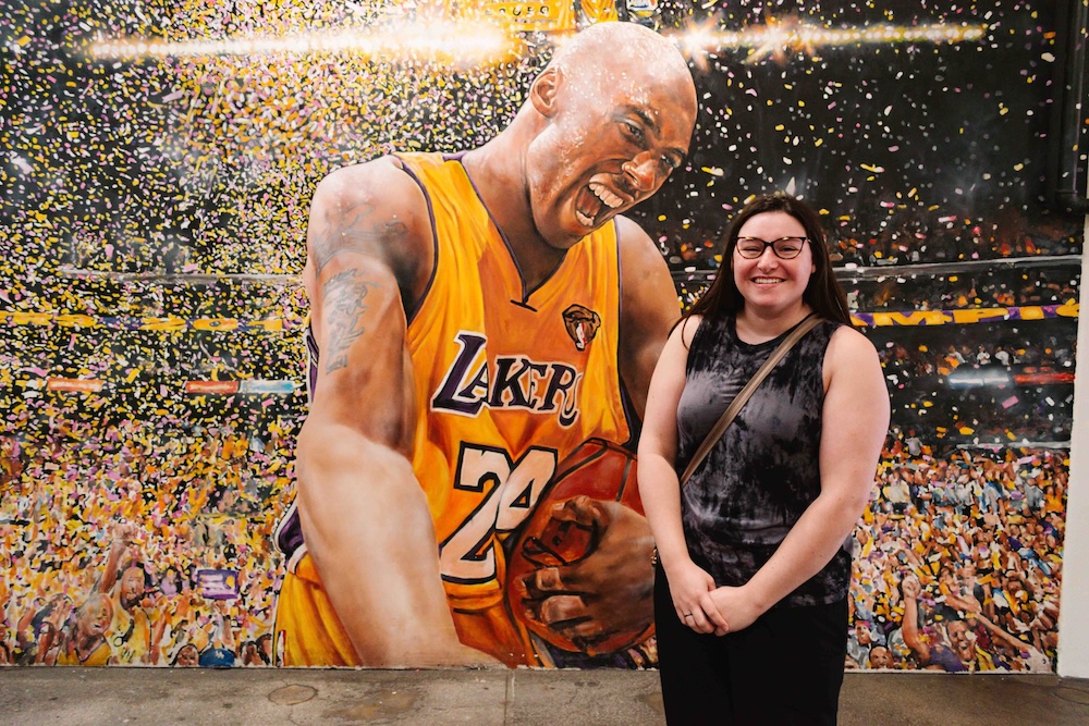 Woman posing in front of a mural of basketball player Kobe Bryant in a food hall in downtown Los Angeles