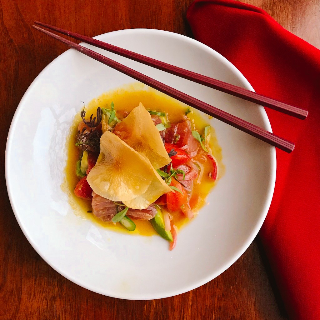 Tuna beautifully plated on a while plate with dark red chopsticks and a deep red napkin to the right side