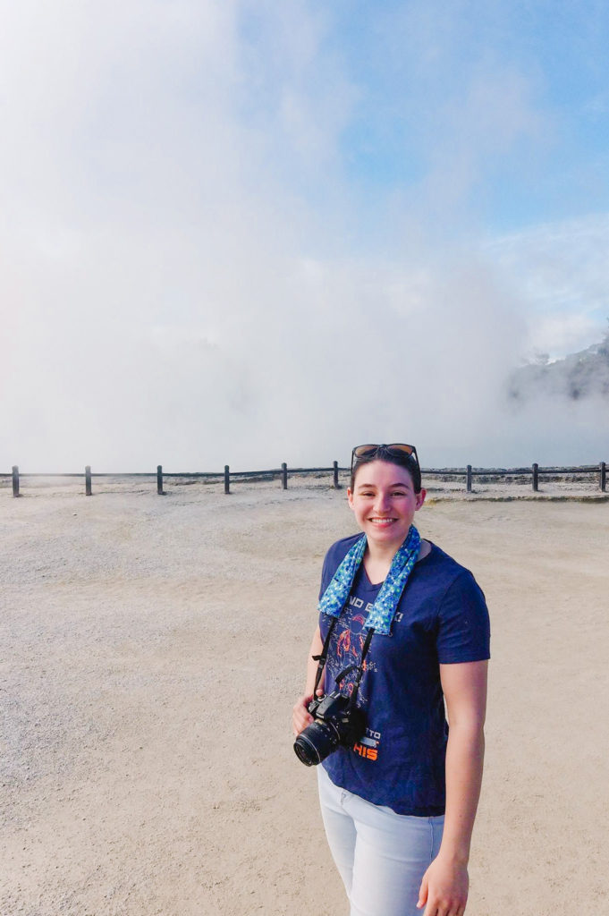 Alanna Koritzke at Wai O Tapu Thermal Park in New Zealand, tan pathway with steam coming off the ground with blue sky