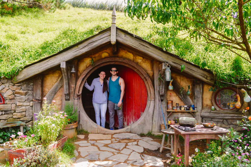 couple posing in a hobbit hole in New Zealand, lush green surrounding