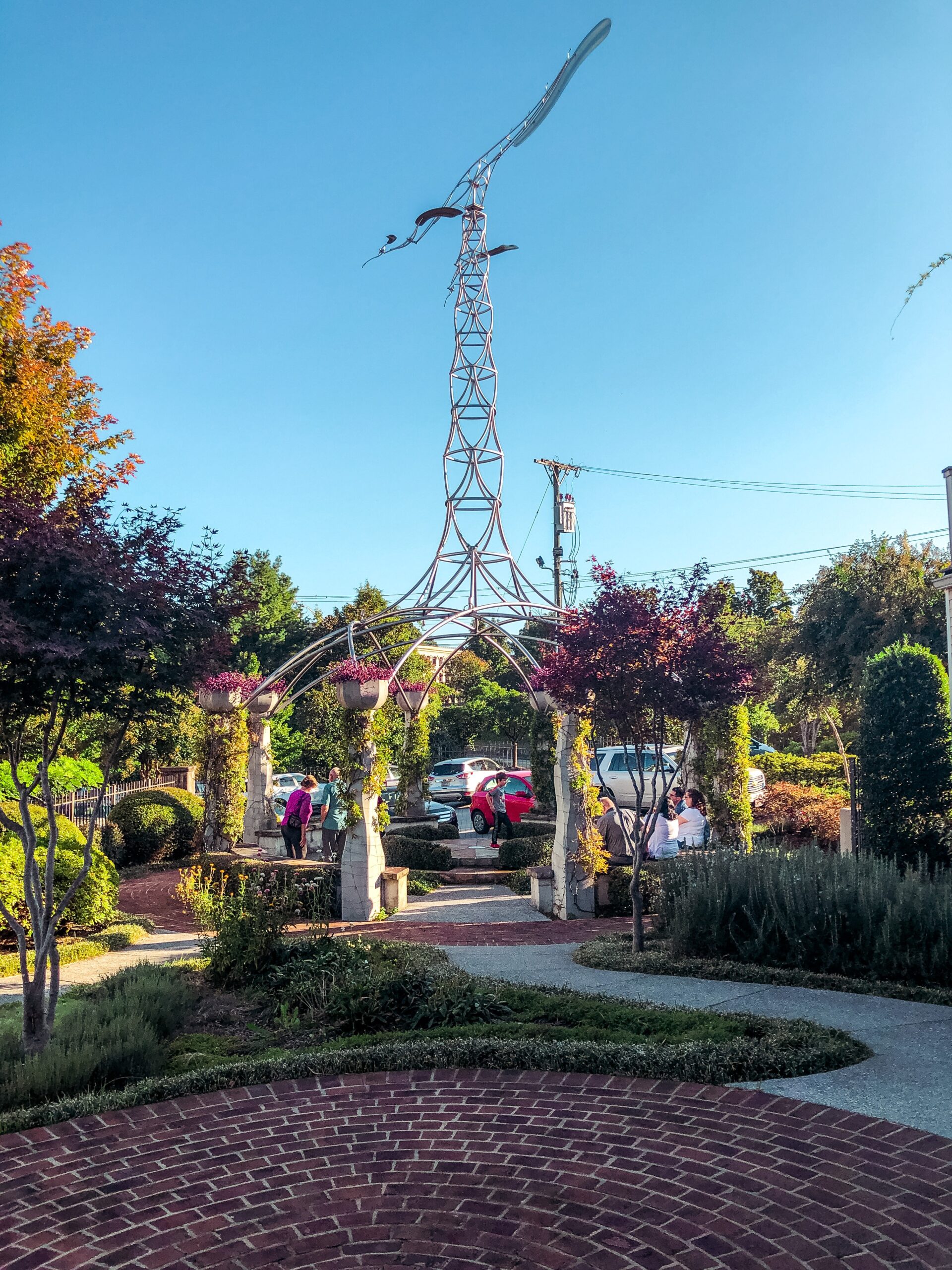 tall statue in a green lush garden with a paved brick and concrete path