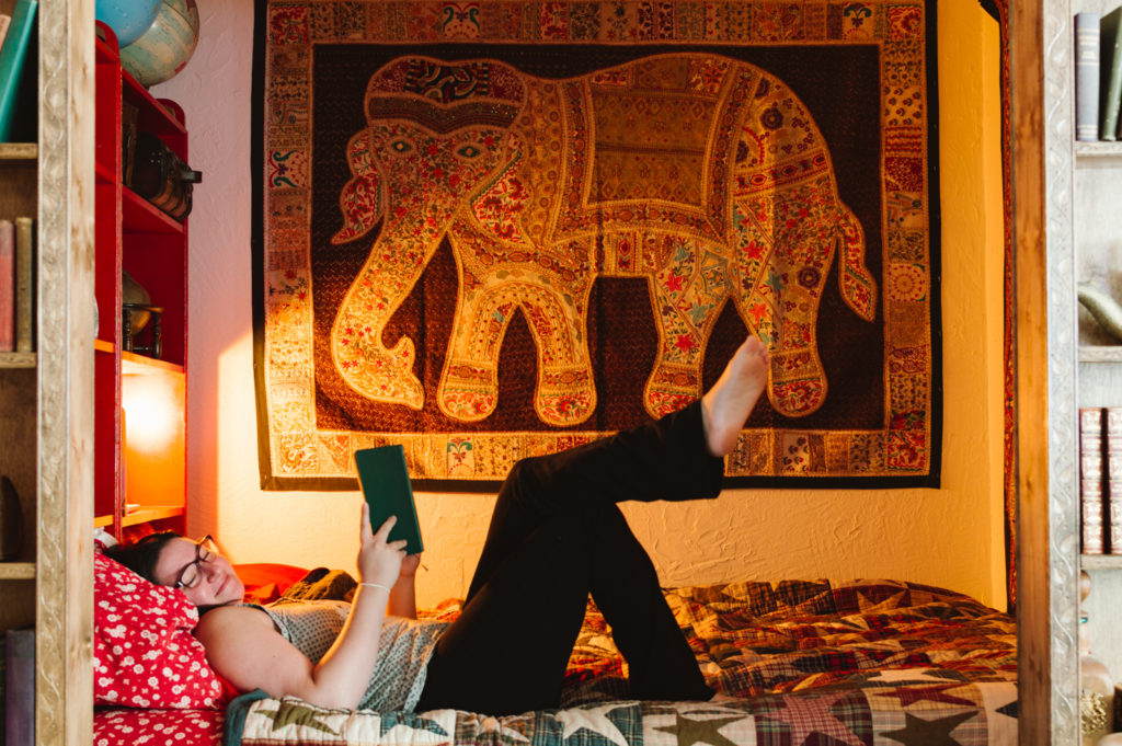 woman laying in bed reading a book with an elephant tapestry in the background