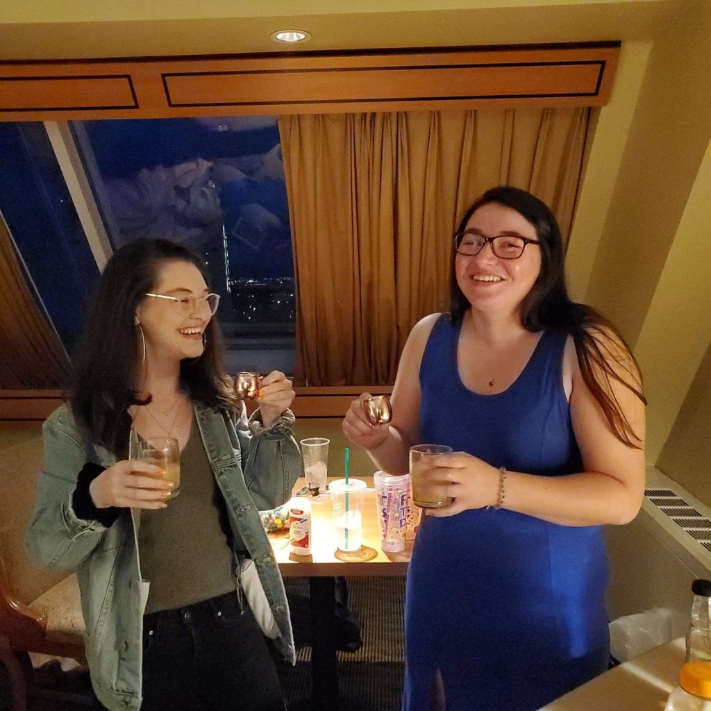 two women laughing and getting ready to take a shot of alcohol in their hotel room