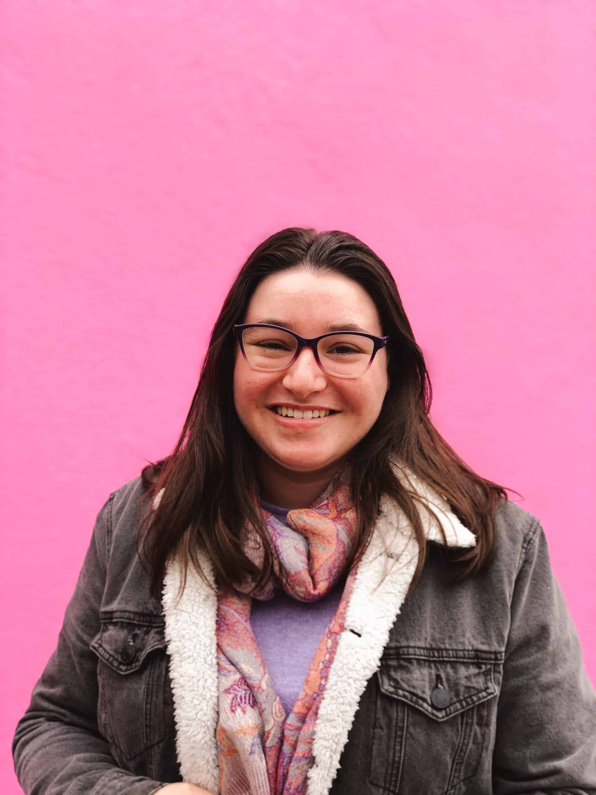Woman smiling to the camera in front of a large pink wall