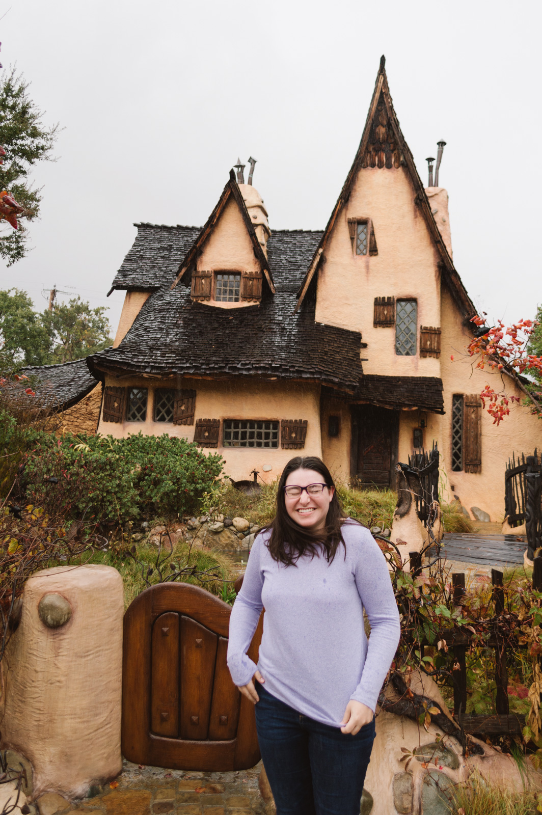 Woman laughing in front of a fairy tale witch's house