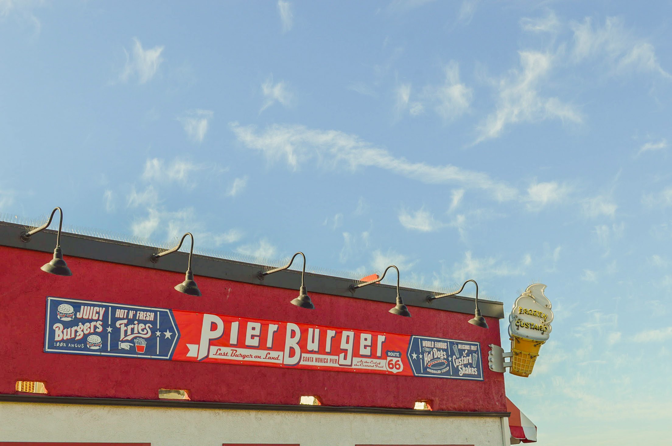 red burger joint with a sign that reads Pier Burger and a neon ice cream cone sticking off the top of the exterior with a sunny blue sky