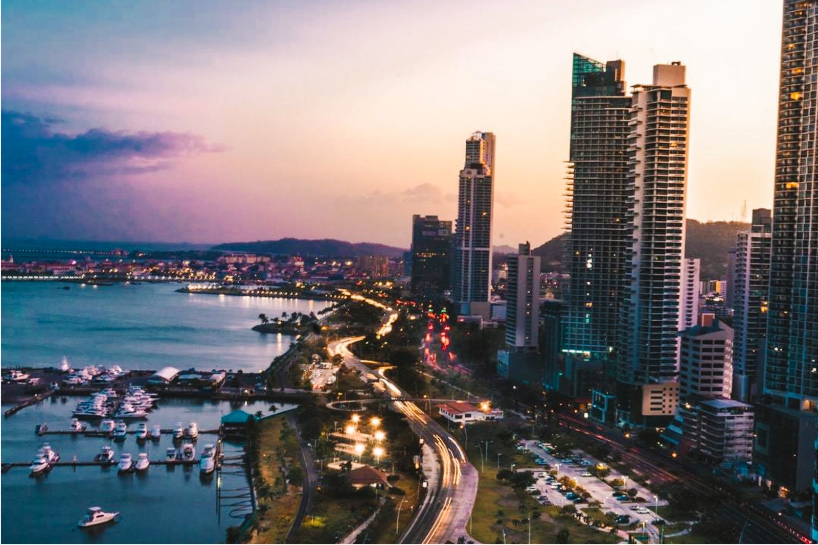Panama City from above with a sunset purple sky and ocean to the left, skyscrapers to the right, road running between ocean/beach and skyscrapers