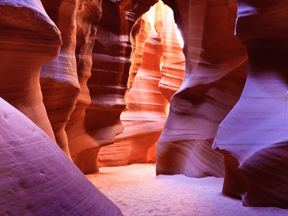 orange red rocks in a slot canyon in Page Arizona with sweeping curves and seemingly smooth surfaces, sunlight coming in from above at the back of the canyon, view from inside the canyon