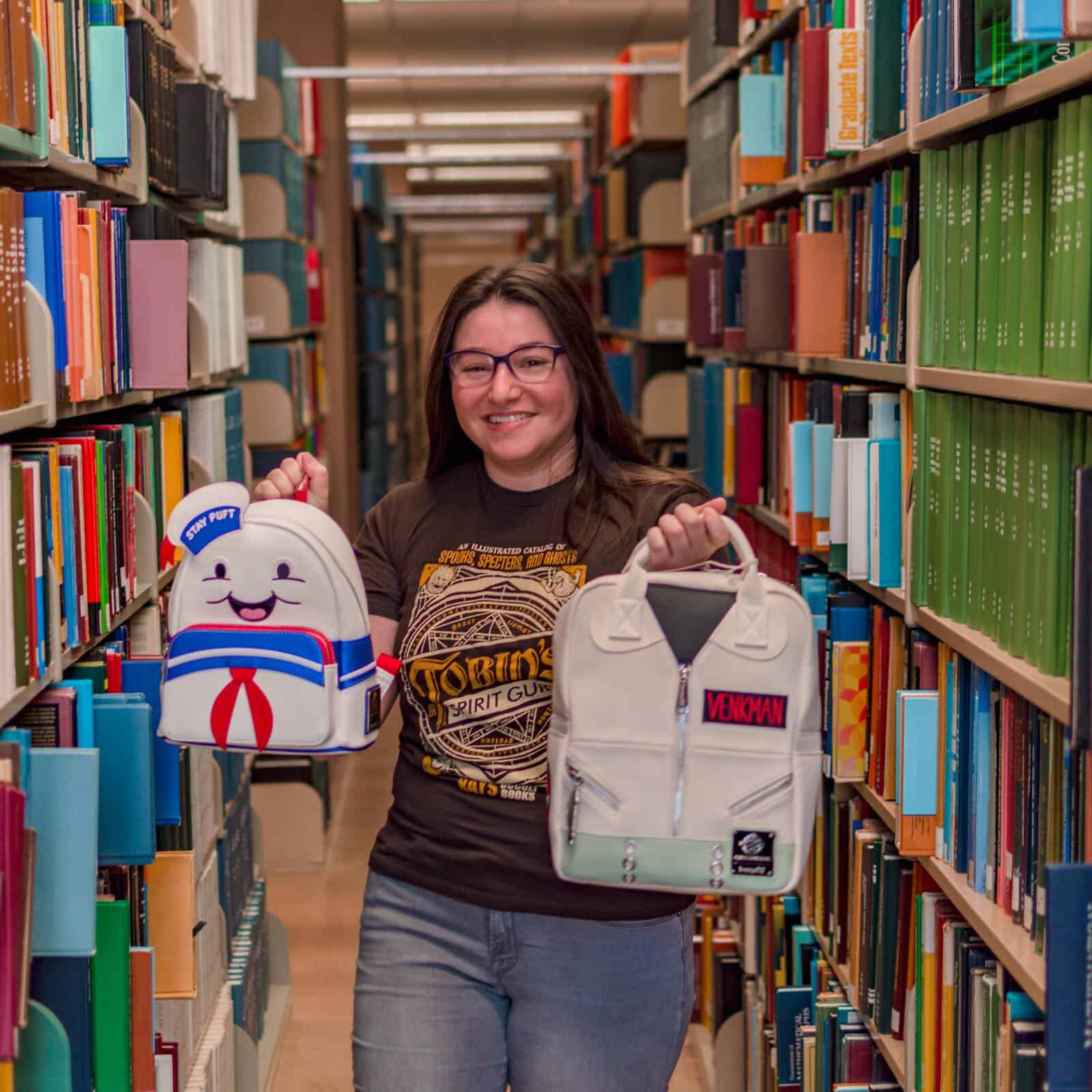 Stay Puft and Venkman mini backpacks held by a woman wearing a Tobin's spirit guide shirt in a library