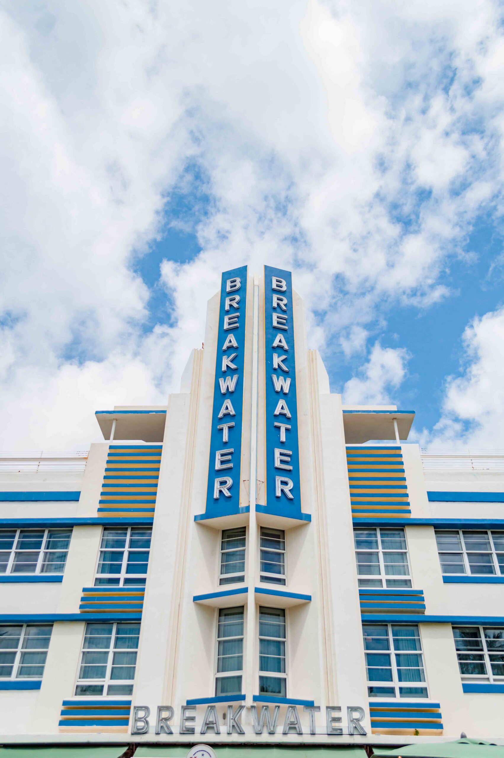 view of a hotel exterior called Breakwater, a white building with blue accents and large vertical Breakwater sign