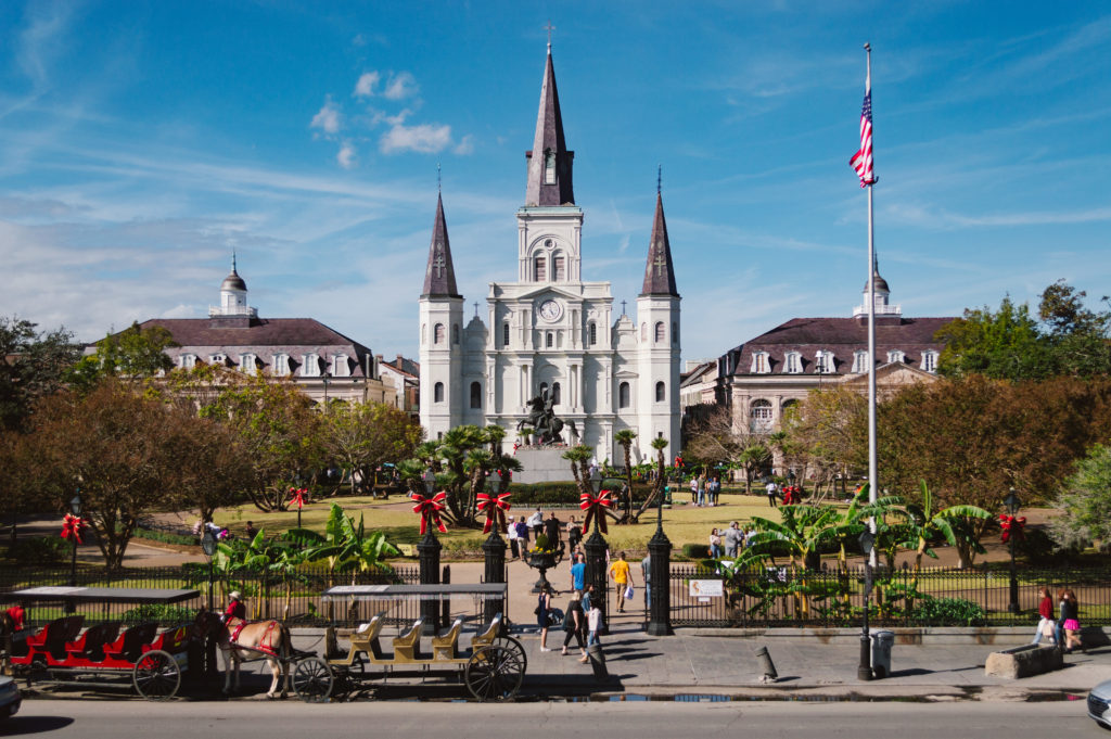 center view of Jackson Square in New Orleans Louisiana with St Louis Cathedral, a tall white church with grey spires, a statue of Andrew Jackson on a horse in the center, and a park surrounding