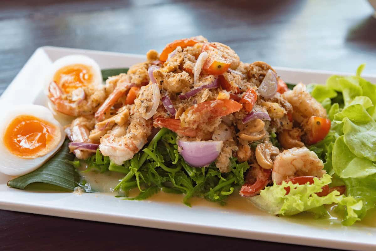thai food piled on a plate with soft boiled eggs to the left and lettuce to the right