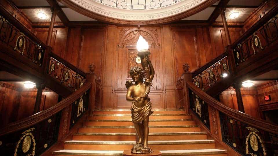 Grand Staircase of the Titanic ship with one main staircase in the center and two staircases leading away to the right and left with an angel statue in the middle