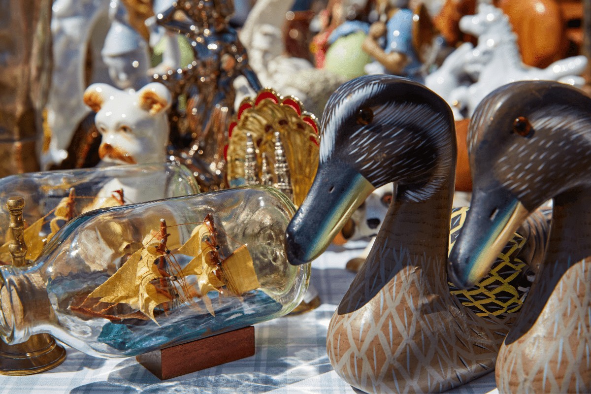 antique duck statues and ships in bottles at an antique market outdoors, closeup of these items on a table