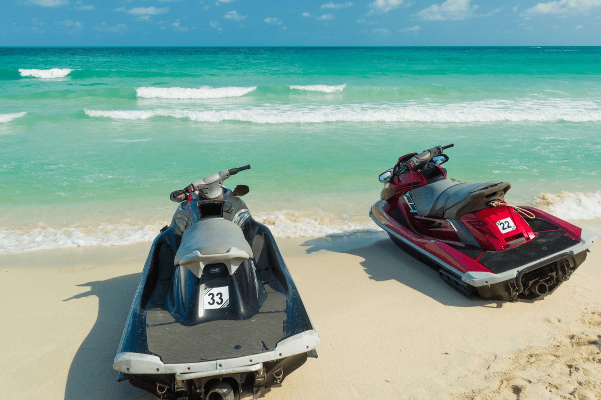 two jet skis, one black and one red, on the beach with turquoise calm water