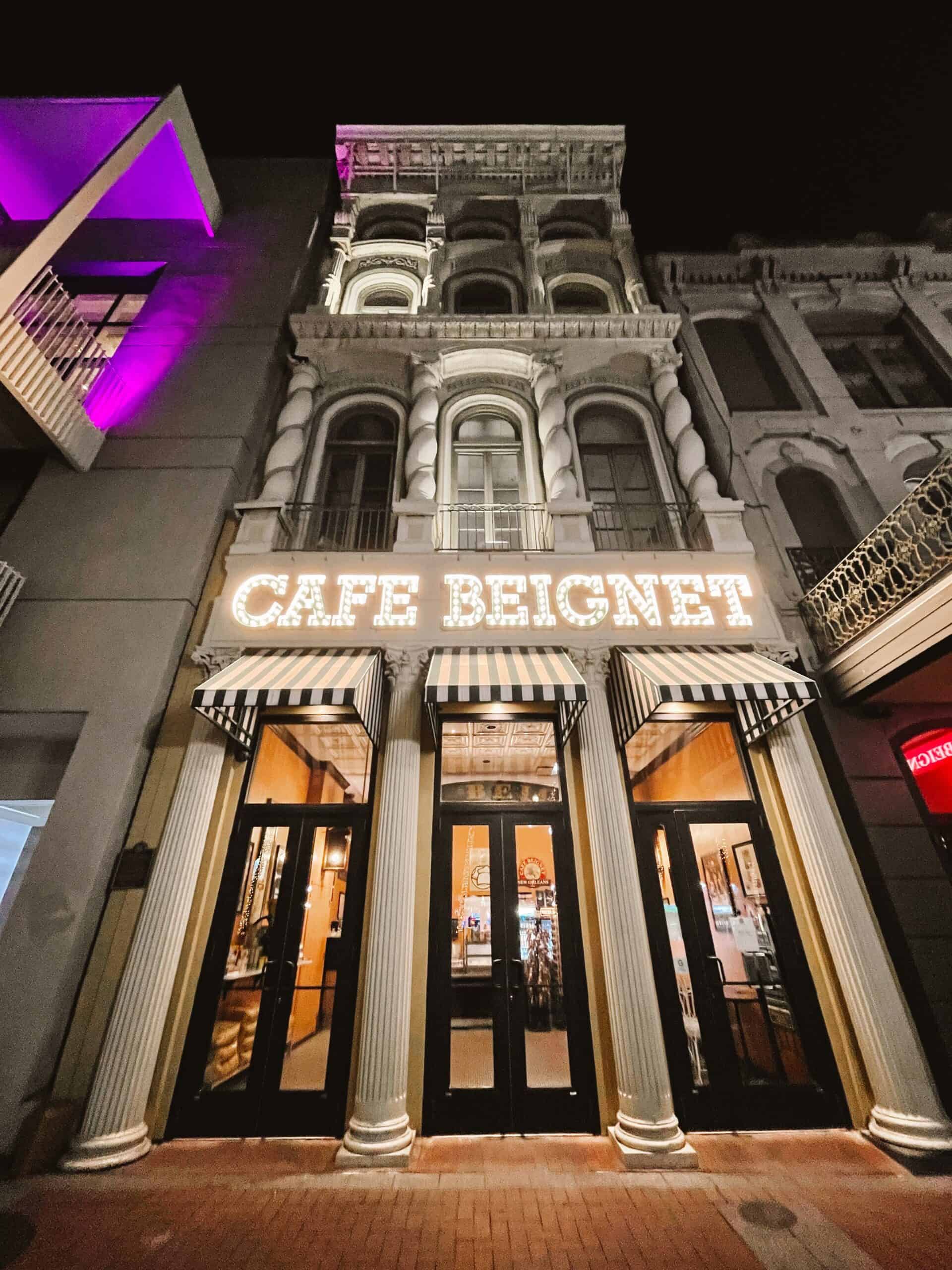 Cafe Beignet at night with neon sign lit up and four pillars at the entrance