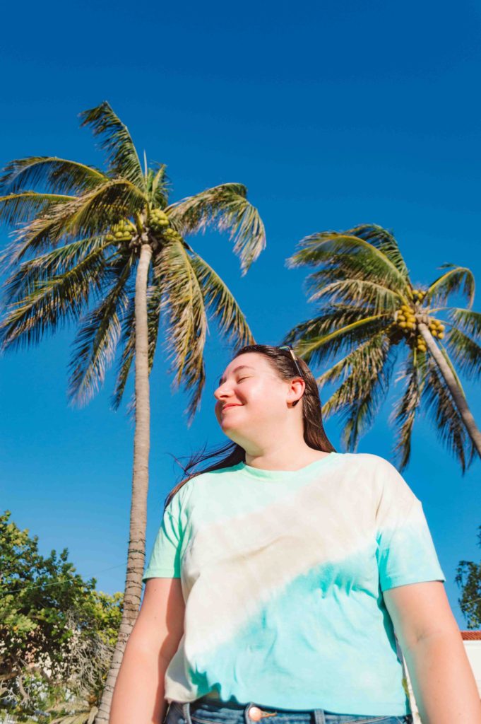 woman looking to her right with palm trees in the background and clear blue skies
