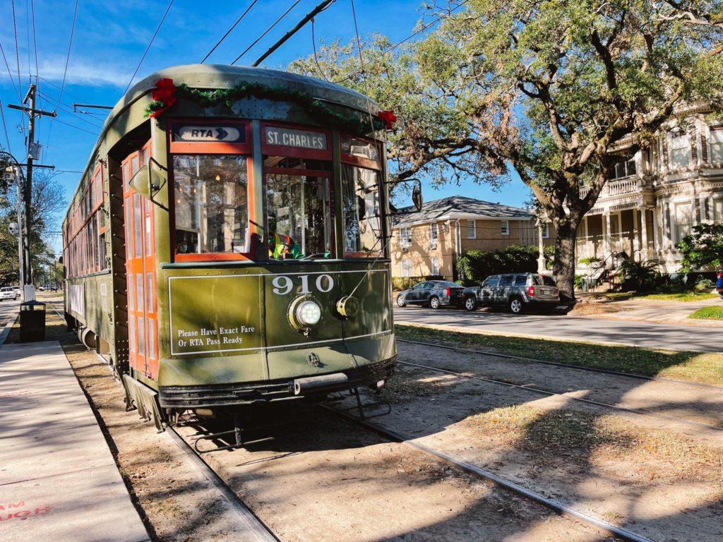 green streetcar on a track with a spanish moss covered tree to the right