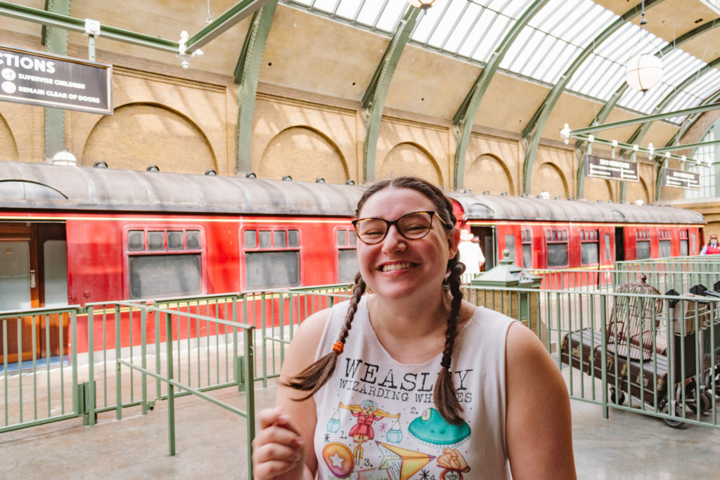 young woman smiling and laughing at King's Cross Station in Universal Wizarding World in Orlando with Hogwarts Express train behind her