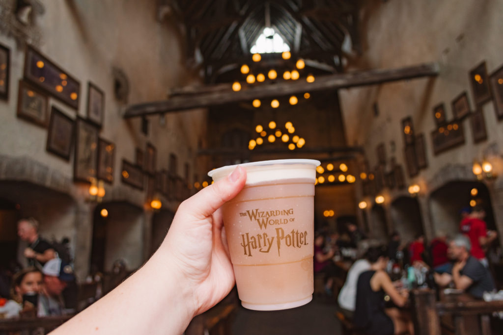 hand outstretched holding frozen butterbeer from the Wizarding World of Harry Potter in Universal Orlando with the Leaky Cauldron restaurant in the background