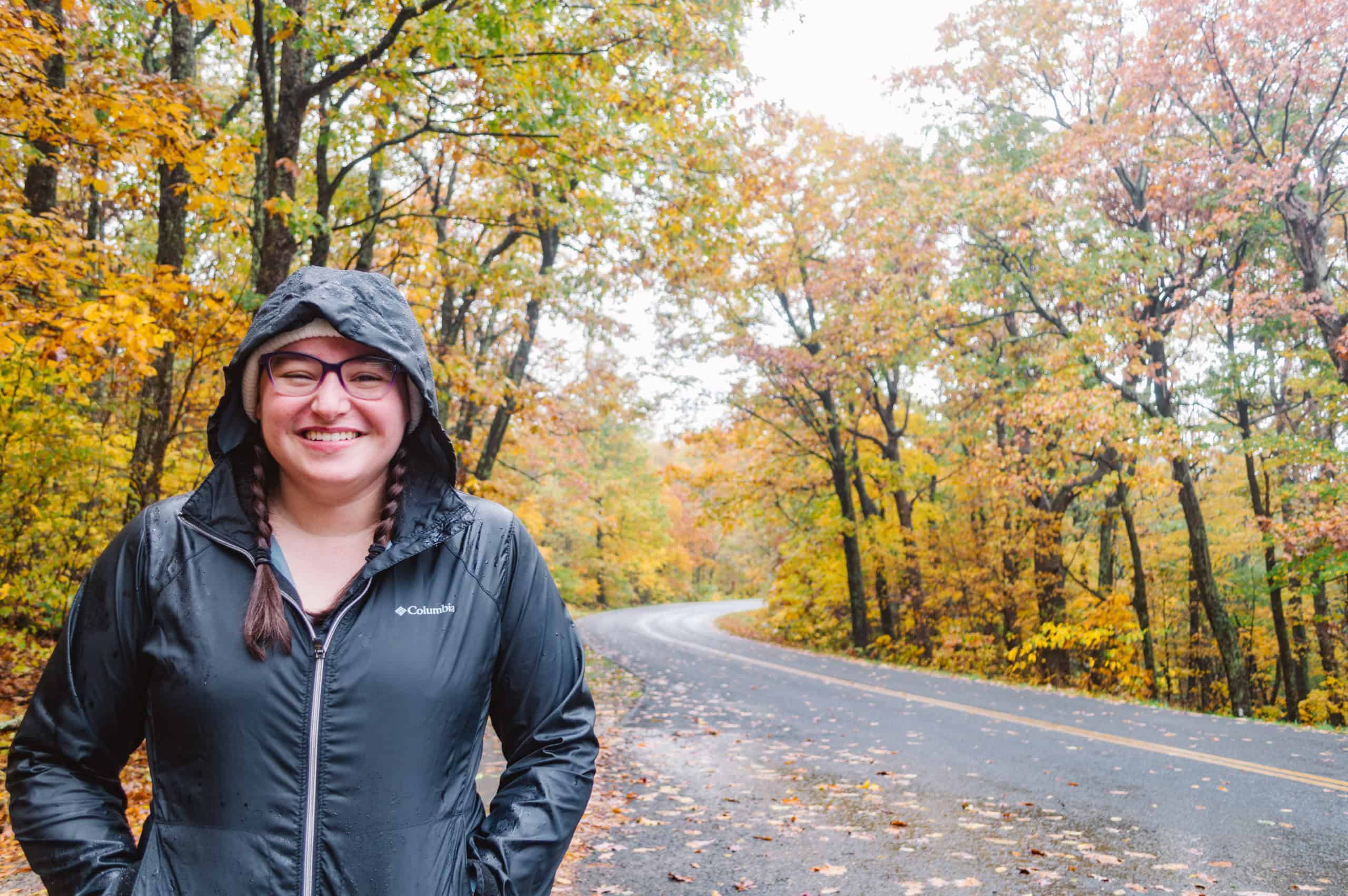 Woman standing along the side of the road in fall in a rainjacket