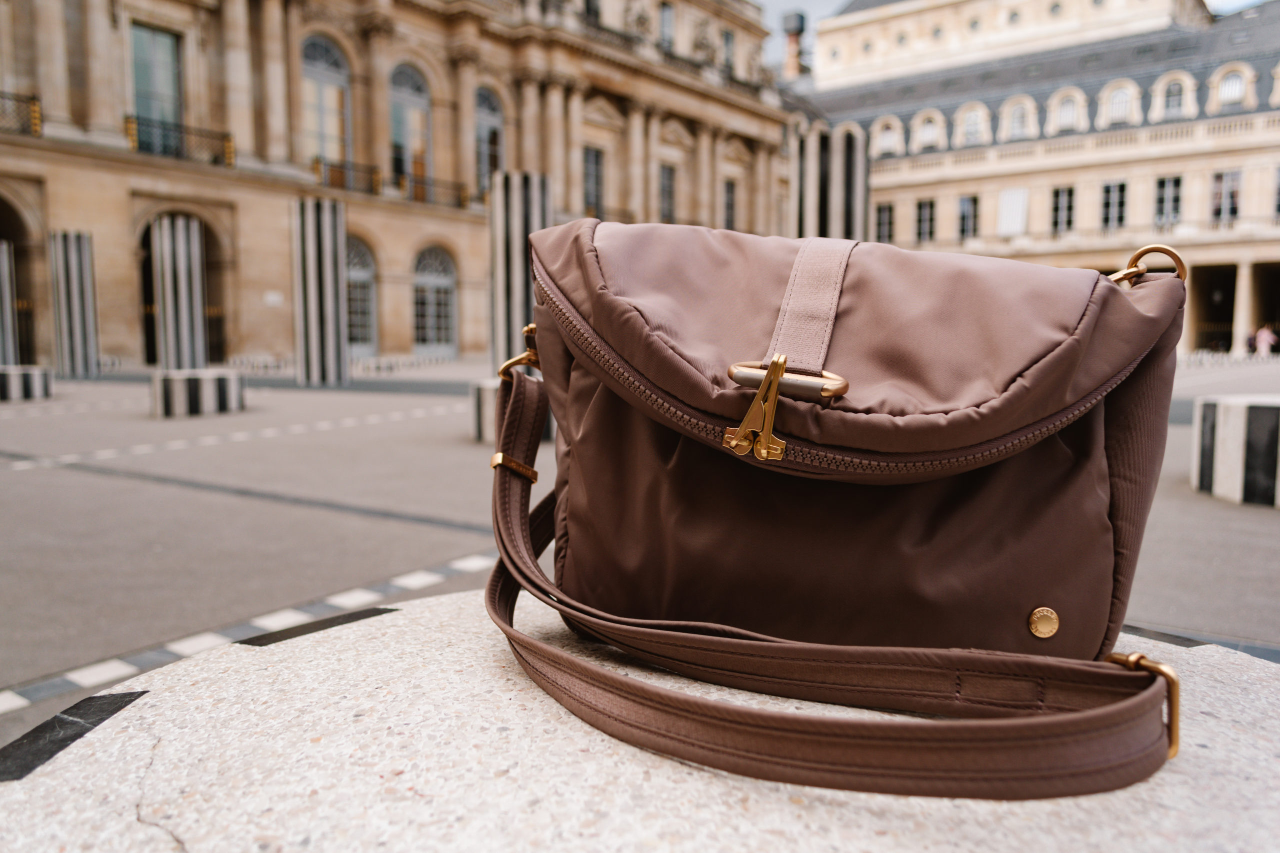 PacSafe convertible bag that is brown in color on a low pillar in Paris
