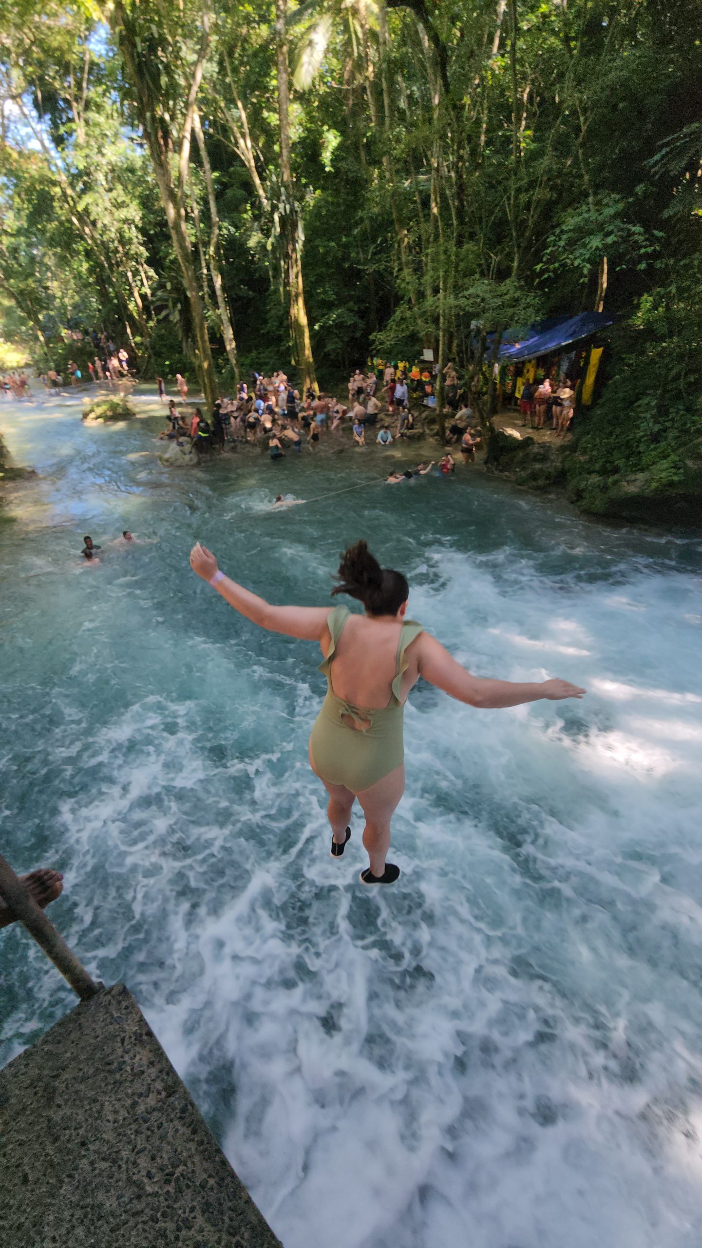 woman in green bathing suit cliff jumping into a rushing pool of water