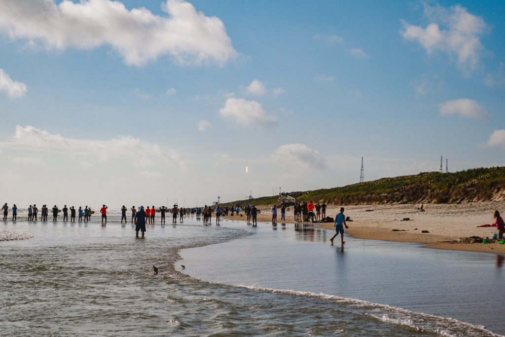 rocket launch off the coast of Cape Canaveral Florida with many people on the beach watching