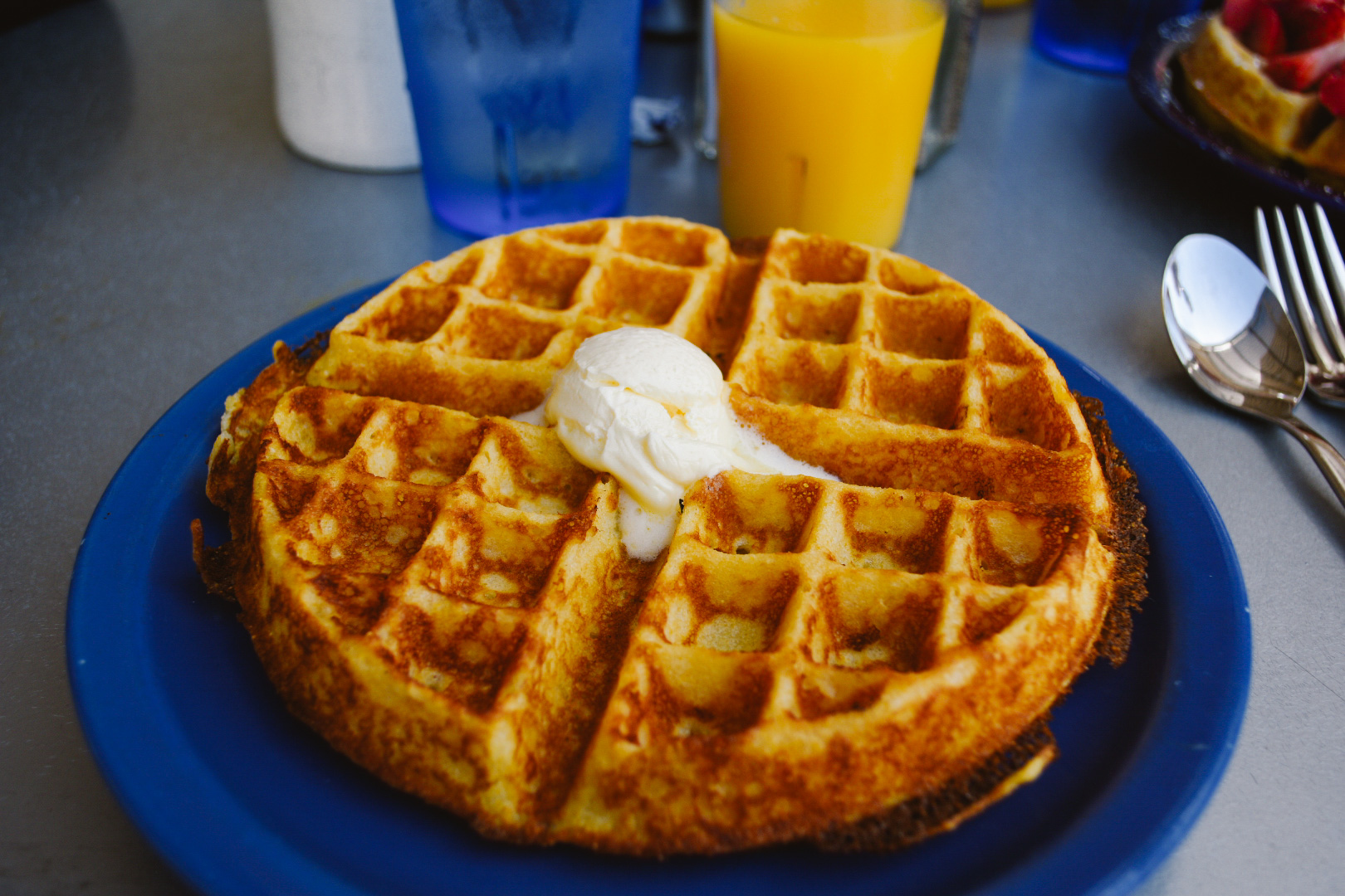 corn waffle with a dollop of butter on top with orange juice and water glasses behind the blue plate