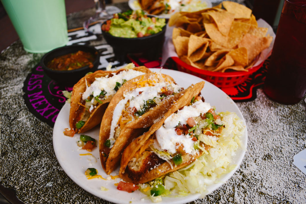 plate of three tacos with chips and quacamole in the background