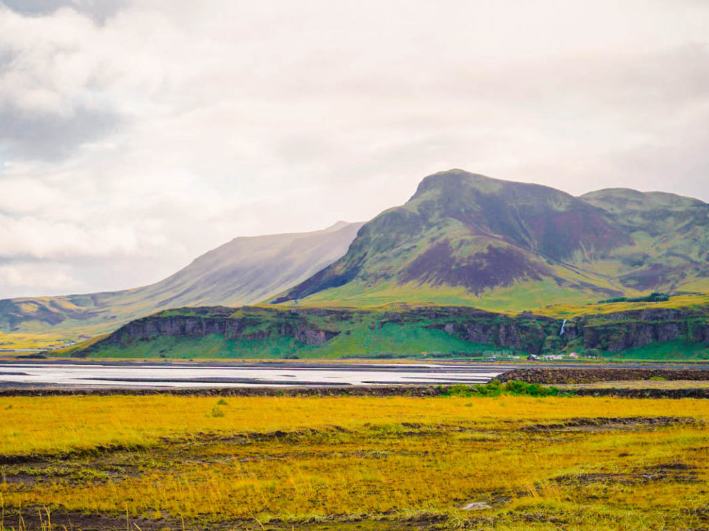 Iceland landscape with mountains in the background, lake in the center, and rolling fields in the foreground