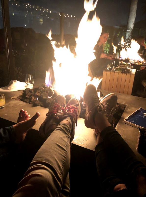 three woman with their feet put up on the edge of a fire pit.