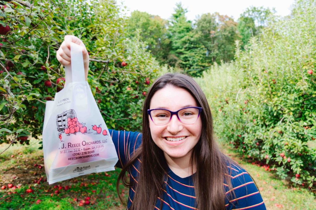 woman holding up a ยฝ peck of apples in an apple orchard in Georgia USA