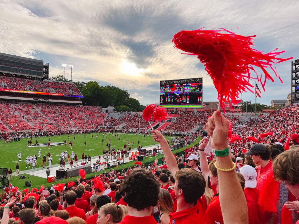 view of a college football game from the student section with red pom poms being waved in the air by students