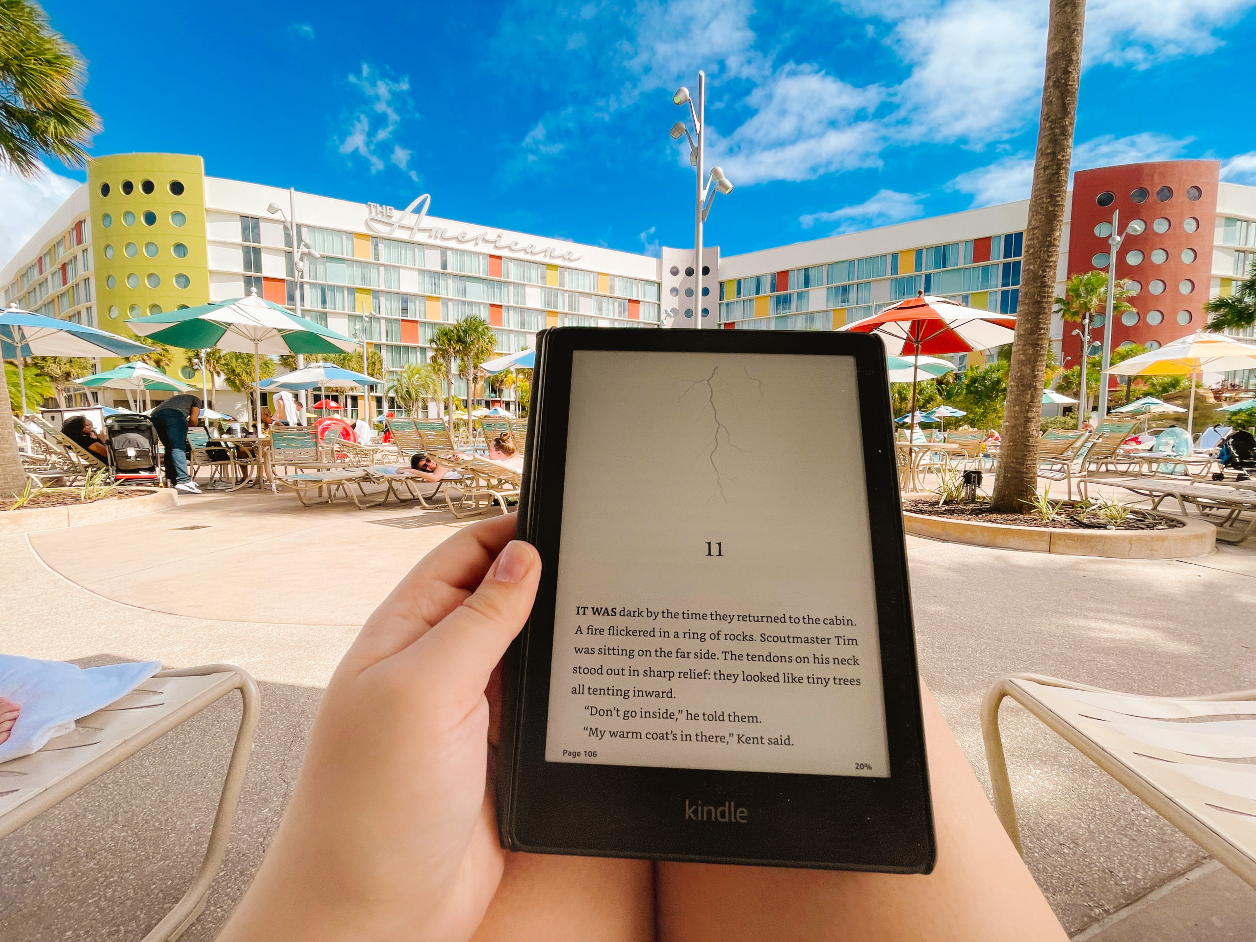 woman's viewpoint of her book in her lap with a retro hotel and pool in front