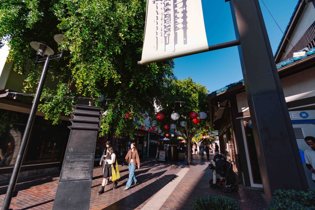 view of a Japanese plaza in Los Angeles with red and white lanterns hanging from trees with bright blue sky in background