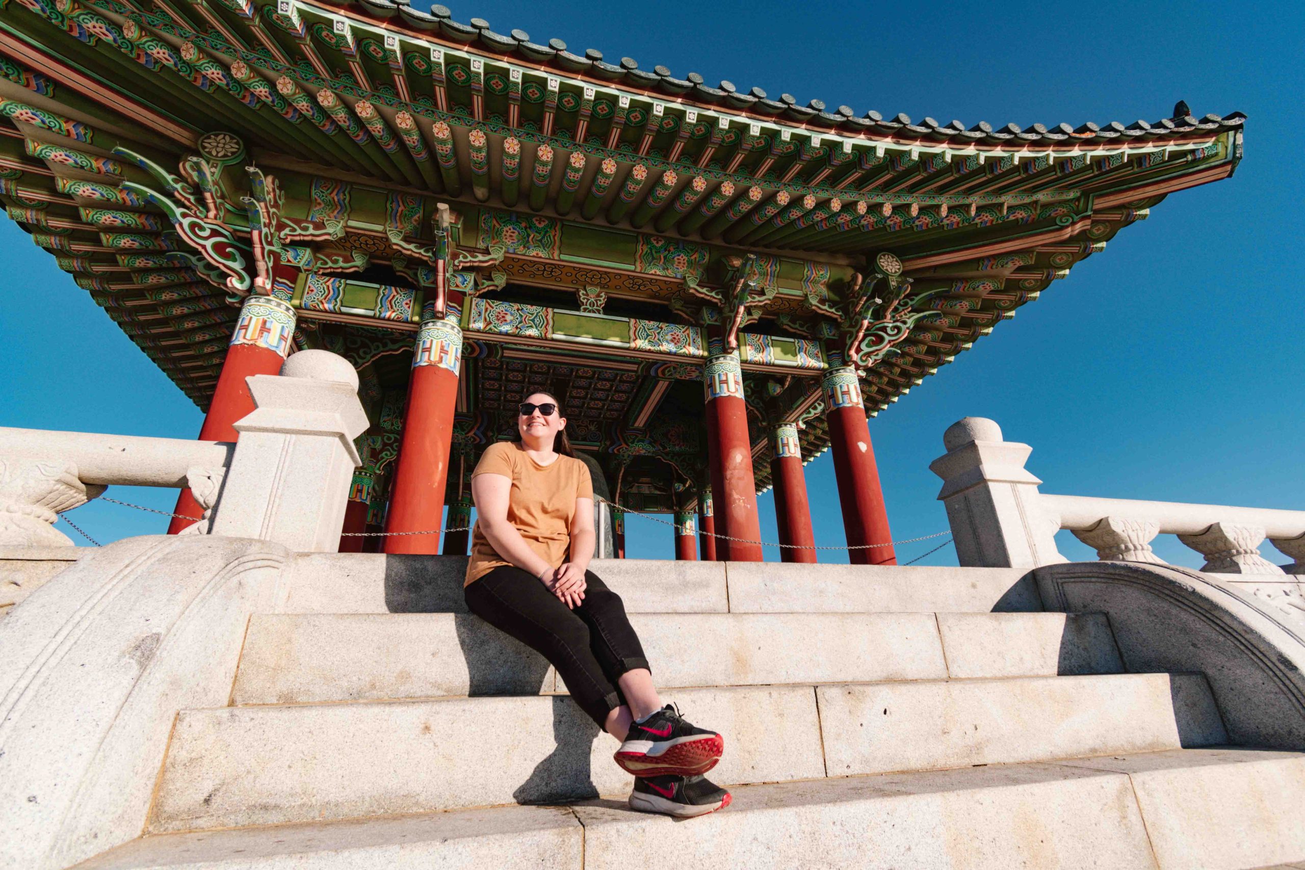 woman sitting on steps leading up to a Korean bell on the coast of Los Angeles