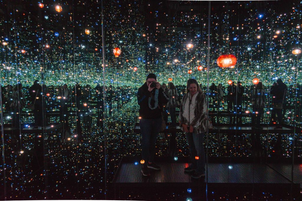 woman and her mother standing inside an infinity mirror art exhibit