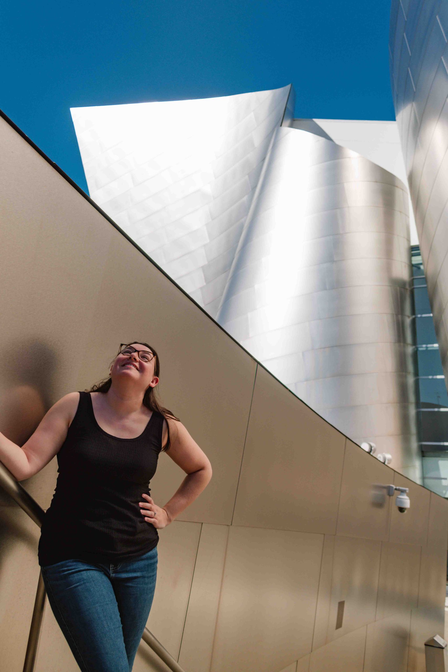 woman looking up standing on stairs at Walt Disney Concert Hall, a Frank Gehry building