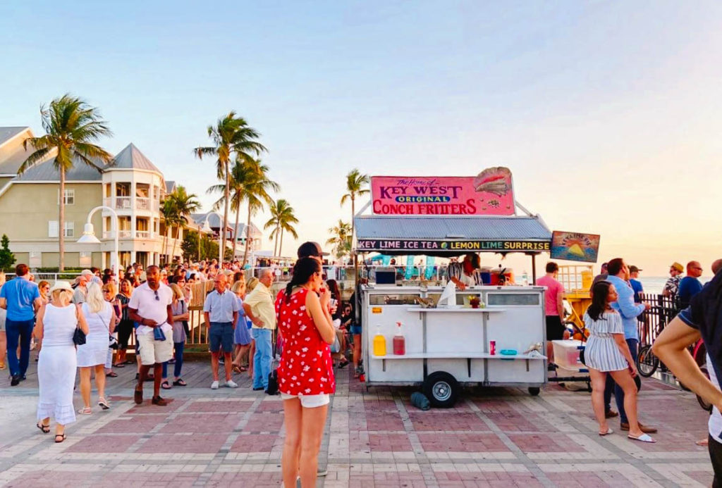 crowd of people at a town square oceanside watching a sunset with a food cart serving snacks in Key West