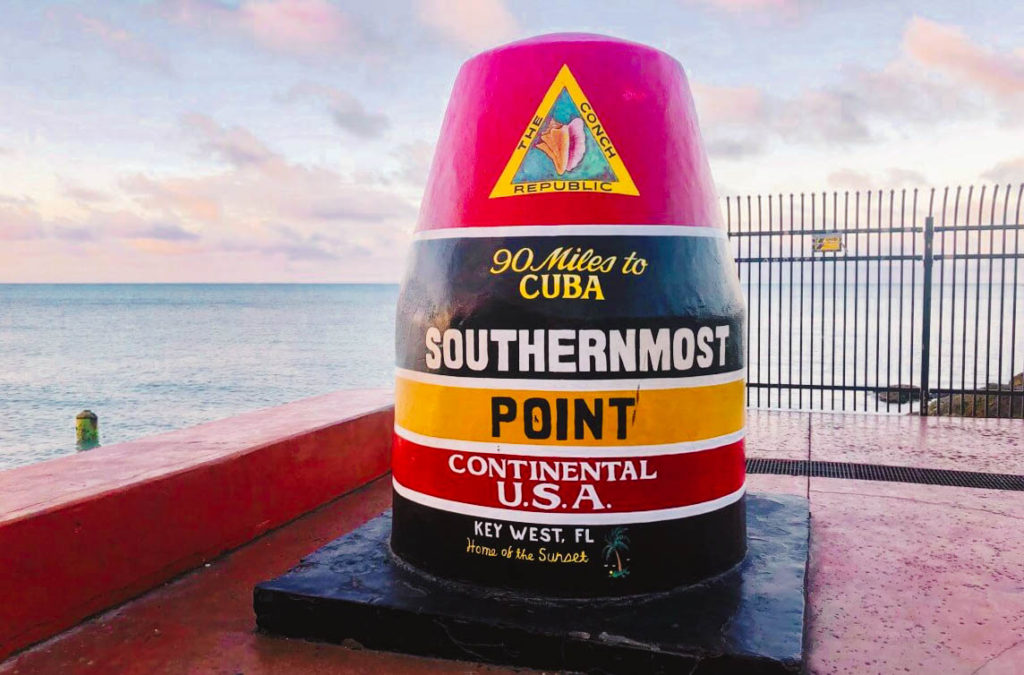Striped buoy on land that represents the Southernmost Point of the continental United States with red, black, orange stripes.