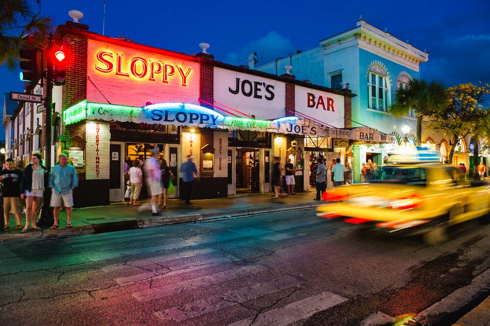 Exterior night shot of Sloppy Joe's Bar in Key West with zooming taxi in the front and lit up neon