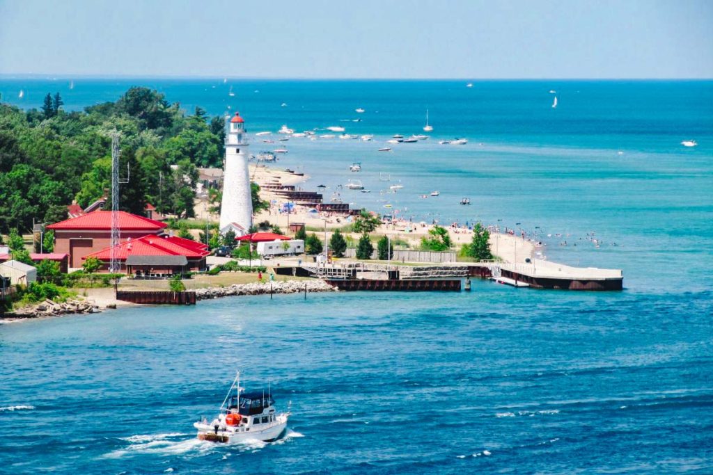 lighthouse and small down on the edge of a cliff coast with a boat traveling toward the shore