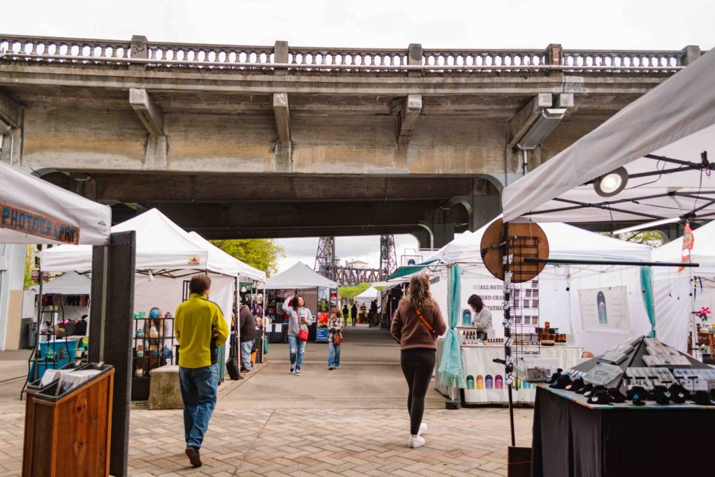Portland Oregon Saturday Market with rows of vendors view from between them with a bridge above