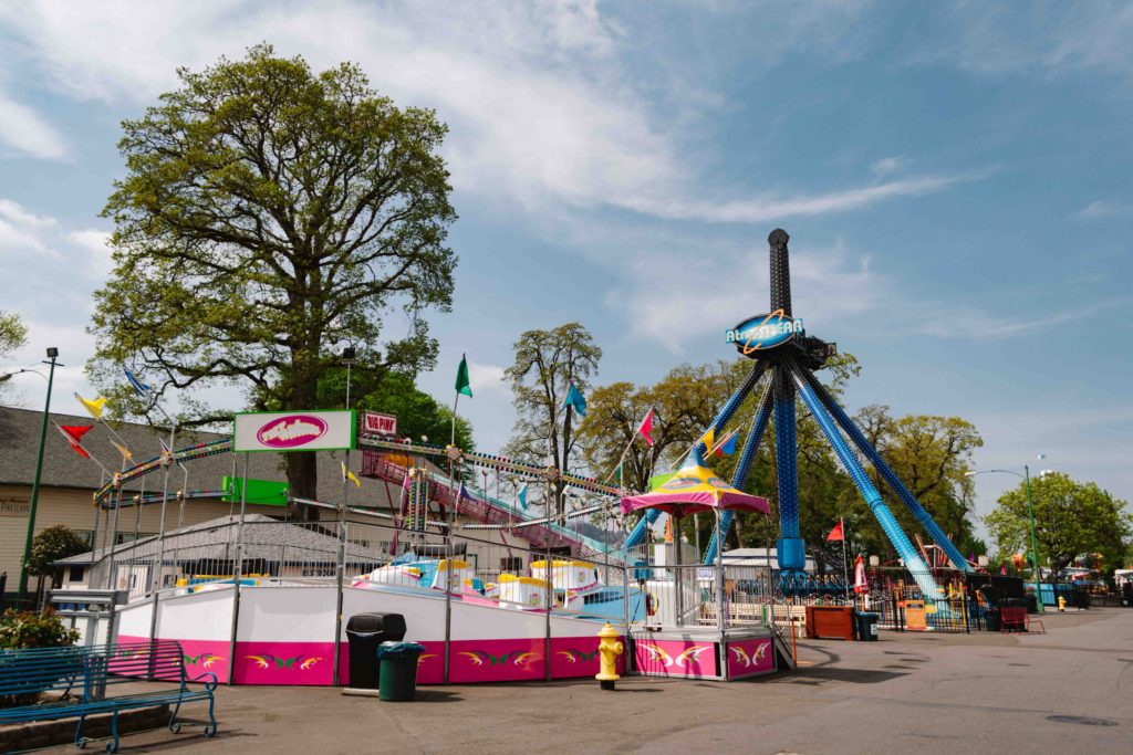 Small amusement park rides on a lot with green trees in the background