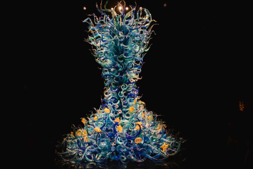 large dark and light blue glass sculpture with cream colored sea creatures interwoven throughout