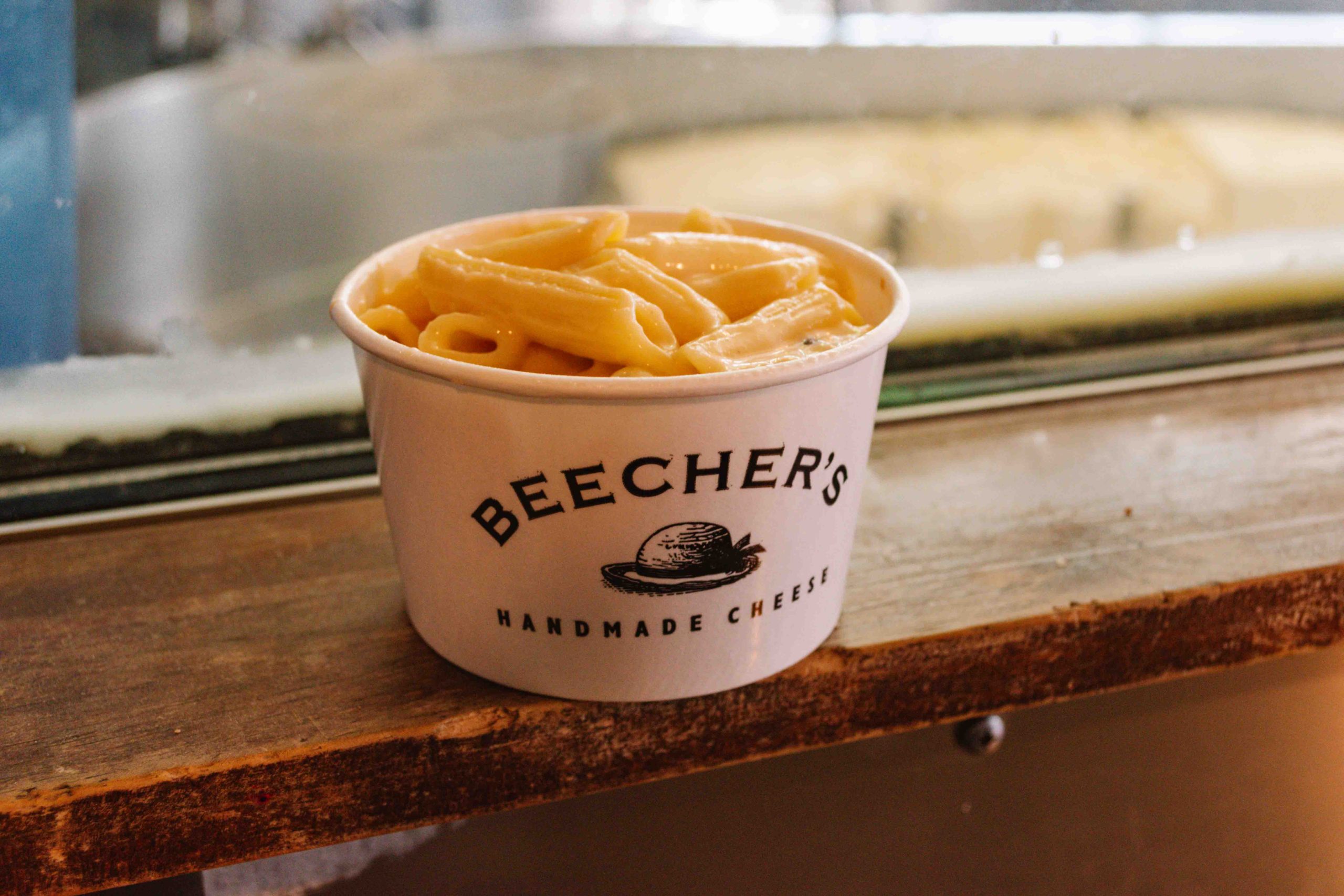 Beecher's Handmade Cheese mac and cheese in a small white cup sitting on a wooden table shelf